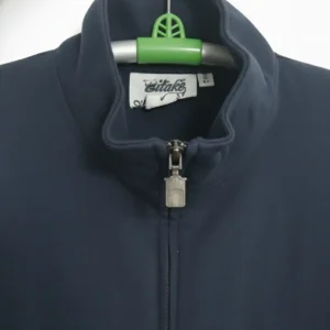 A navy blue full-zip jacket with a high stand collar, ribbed cuffs, and a small square patch logo on the upper left sleeve, photographed on a hanger.